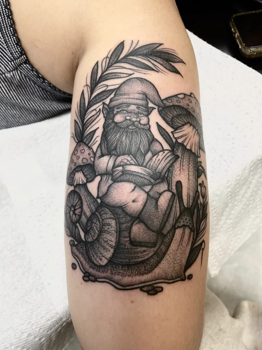 Black and grey stippled illustrative gnome with mushrooms and a snail, tattooed on an arm by Josh Espenschied at True North Tattoo in Lancaster, PA