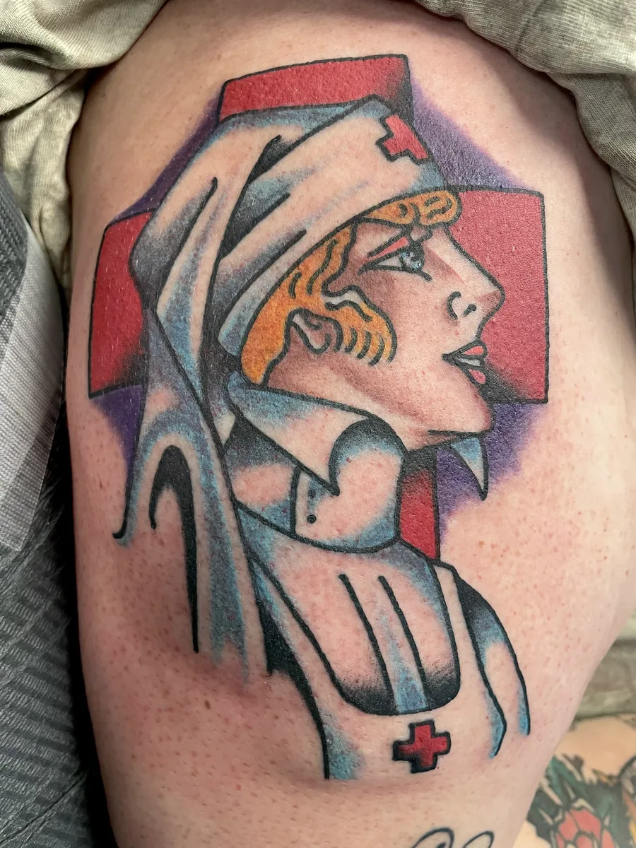 Traditional nurse pin-up tattoo with a red cross background on an upper arm by Josh Espenschied at True North Tattoo in Lancaster, PA
